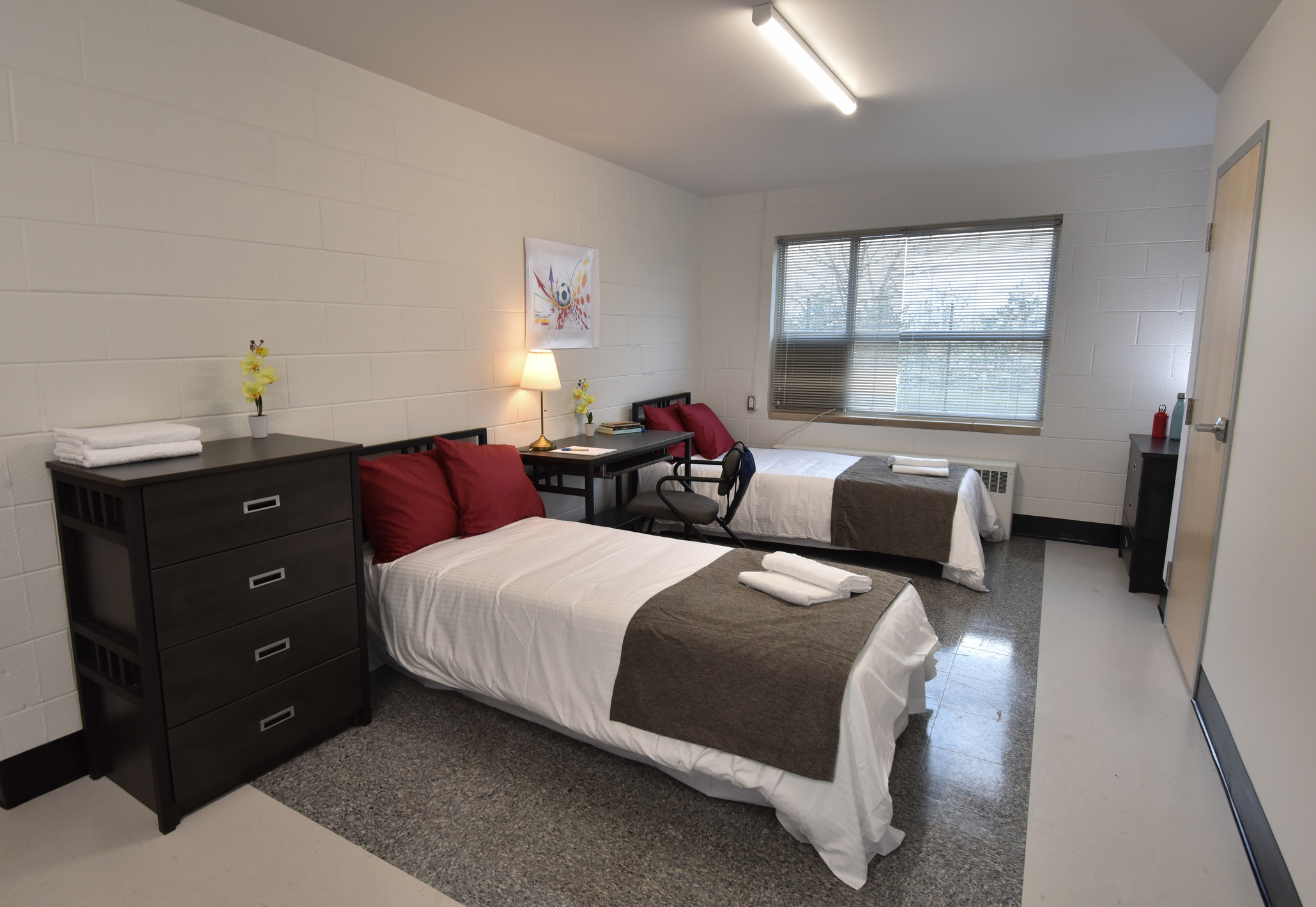 Quarto da residência estudantil da Assumption College com duas camas, mesa de estudo e janela ampla